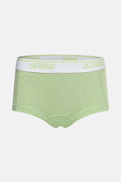Shorty vert de PIECES®, avec une bande élastique blanche portant l'inscription 'SATURDAY'.