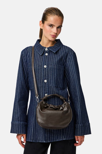 Sac à main brun de PIECES®, avec une poignée nouée et porté avec une longue bandoulière, sur une jupe rayée.