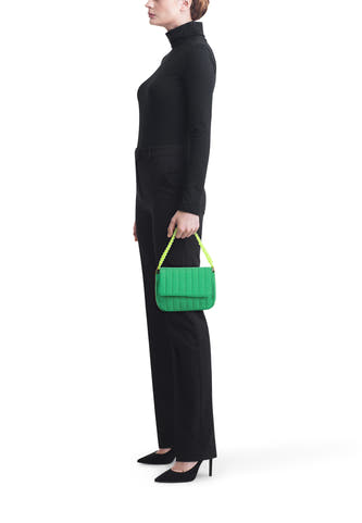 Sac à bandoulière matelassé vert de PIECES avec anse tressée jaune fluo, tenu par un mannequin en noir.