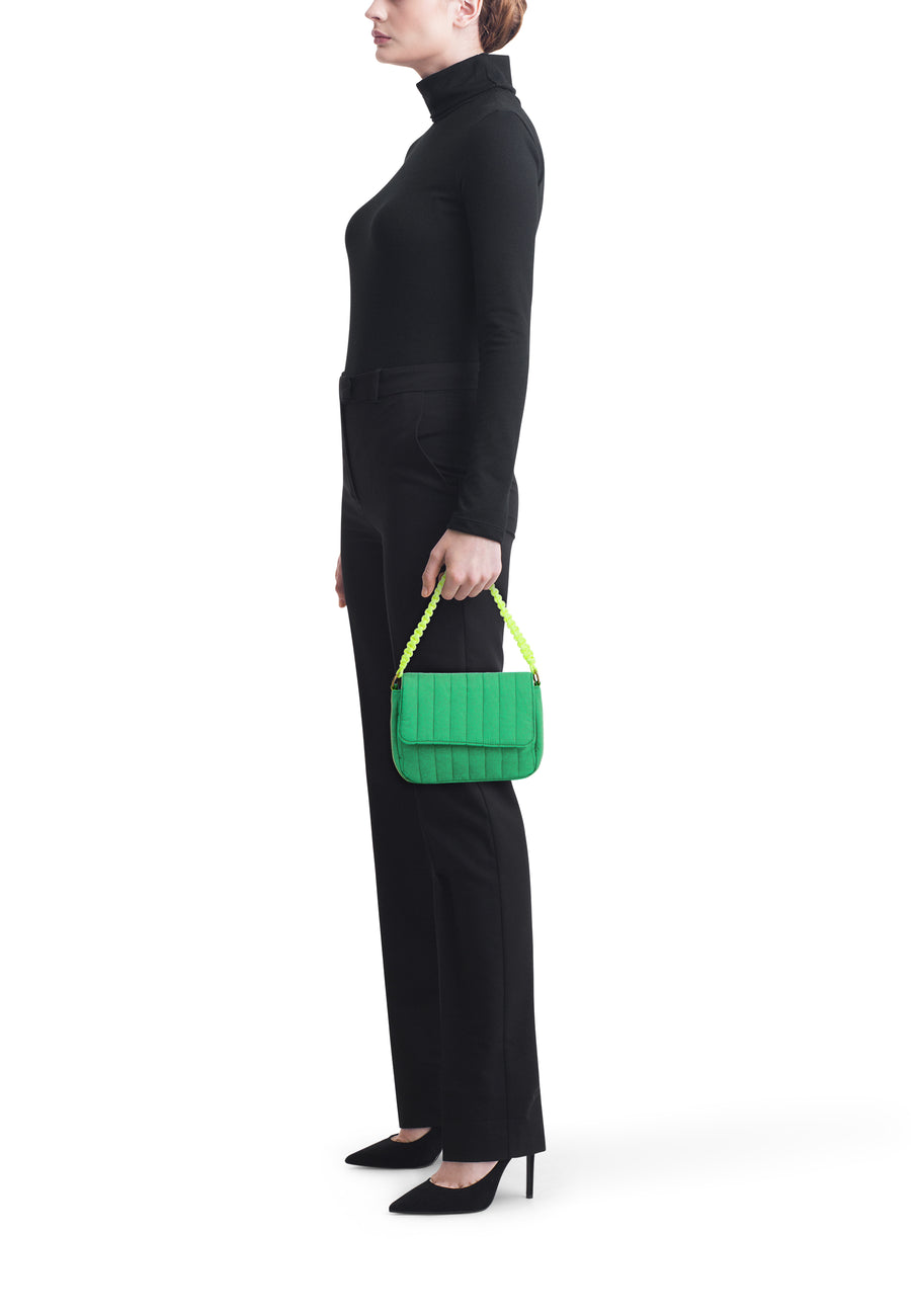 Sac à bandoulière matelassé vert de PIECES avec anse tressée jaune fluo, tenu par un mannequin en noir.