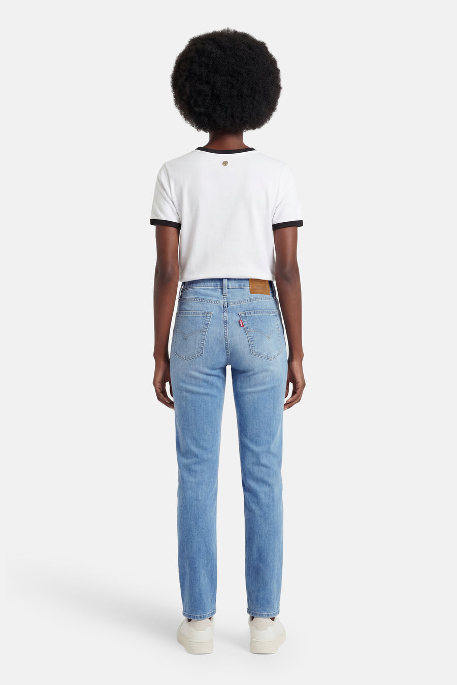 Rechte jeans van lichtblauw denim van Levi's®, met rode merkbadge en model met witte top en sneakers.
