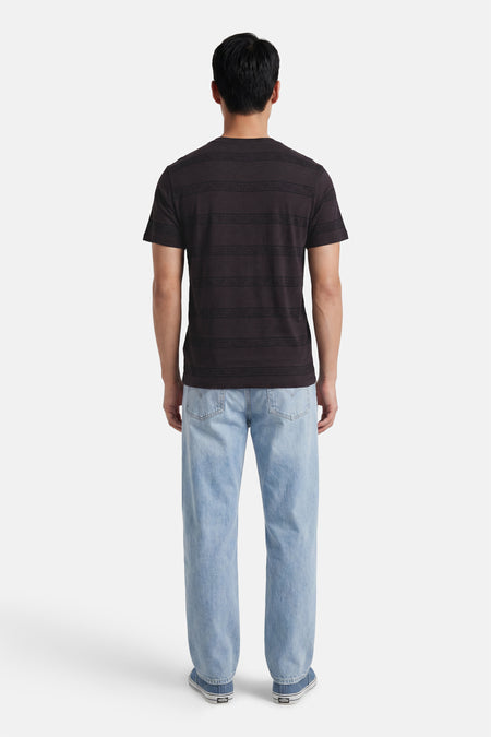 Zwart T-shirt met korte mouwen van Levi's® met horizontale banden en patronen, gedragen door een man, achterkant, met lichte spijkerbroek en blauwe sneakers.