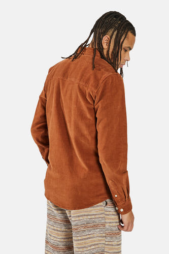Chemise orange à manches longues de REDEFINED REBEL, avec une texture corduroy et portée avec un pantalon imprimé.