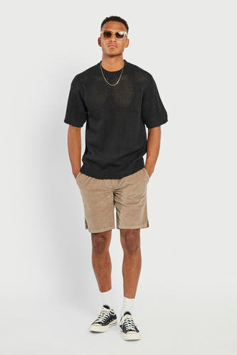 Short marron de REDEFINED REBEL avec poches, combiné avec un pull noir en maille, une chaîne dorée et des lunettes de soleil.