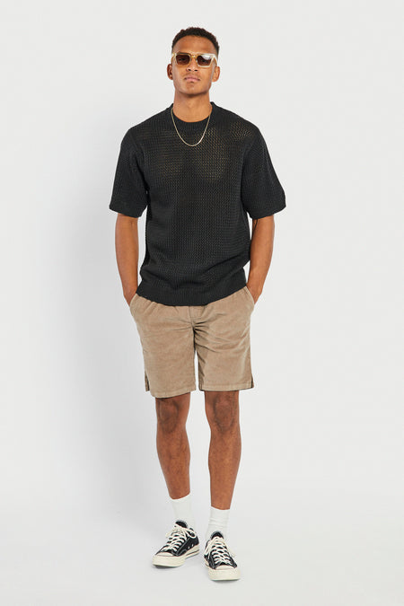 Short marron de REDEFINED REBEL avec poches, combiné avec un pull noir en maille, une chaîne dorée et des lunettes de soleil.