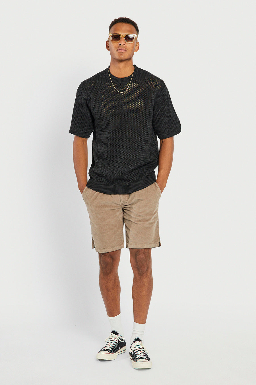 Short marron de REDEFINED REBEL avec poches, combiné avec un pull noir en maille, une chaîne dorée et des lunettes de soleil.