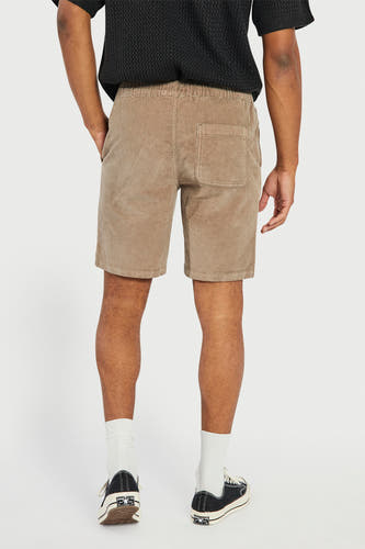 Short marron de REDEFINED REBEL avec poche arrière et taille élastique, porté avec des chaussettes blanches et des baskets noires.