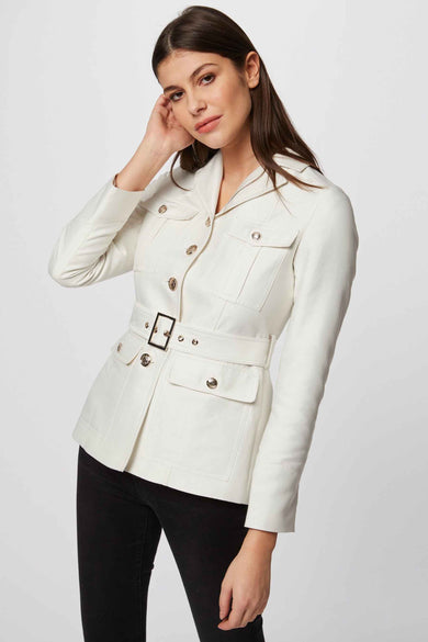 Manteau court blanc de Morgan De Toi, avec ceinture, associé à des jeans skinny noirs et des sandales ouvertes.
