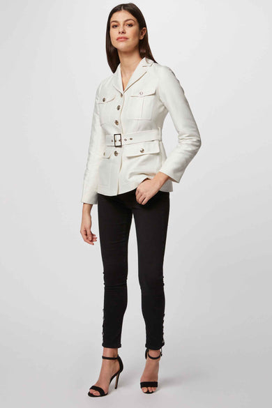 Manteau court blanc de Morgan De Toi, avec ceinture et poches, porté avec un pantalon noir et des bottes.