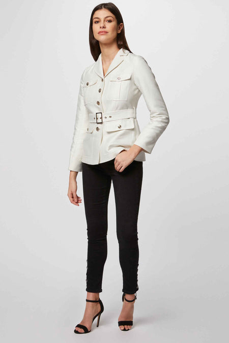 Manteau court blanc de Morgan De Toi, avec ceinture et poches, porté avec un pantalon noir et des bottes.
