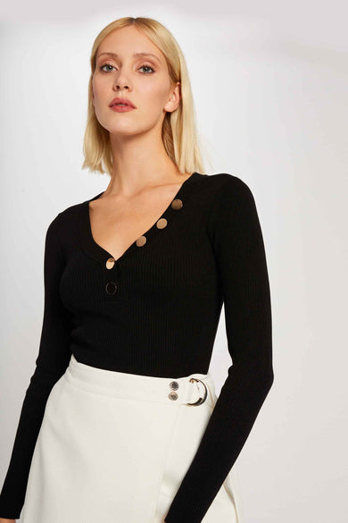 Pull noir à col V de Morgan De Toi, avec des boutons dorés et porté avec une jupe blanche.