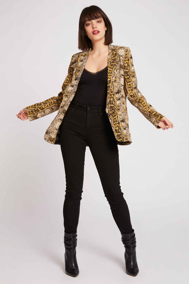Blazer multicolore de Morgan De Toi, avec imprimé serpent, associé à une chemise noire, un pantalon noir et des bottes noires.