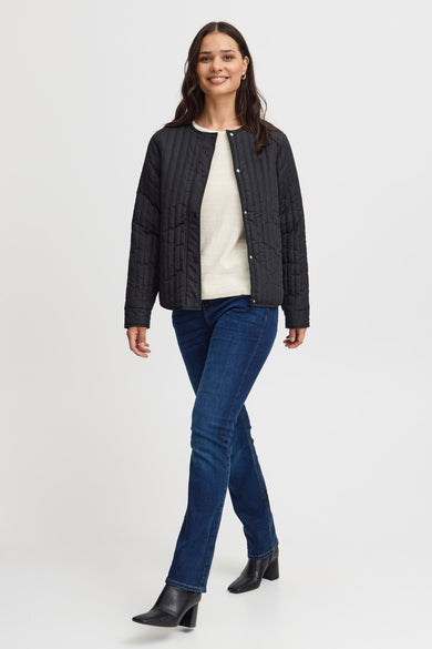 Manteau court noir de France, avec un motif de lunettes intégré, porté sur une chemise blanche et des jeans bleus foncés avec des bottes.