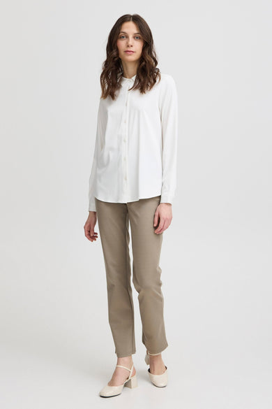 Chemise blanche à manches longues de France, portée avec des pantalons marron et des chaussures crème.