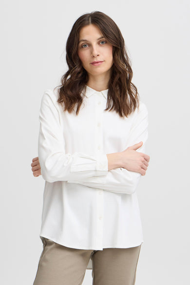 Blouse blanche à manches longues de France, avec collet et portée avec un pantalon beige.