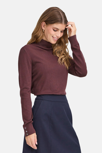 Collier rouge de France, avec des manches longues à détails de boutons, associé à une jupe bleu foncé.