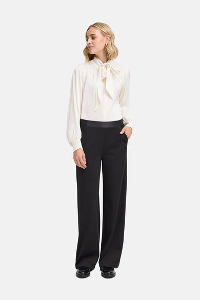Blouse écru avec des manches longues en France, avec un détail de côtes et portée avec un pantalon noir.