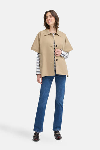 Beige jas van Fransa, met korte mouwen, gedragen over een gestreepte top en blauwe jeans.
