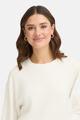 Pull-over blanc de France, avec col rond et coupe décontractée, porté avec des boucles d'oreilles dorées.