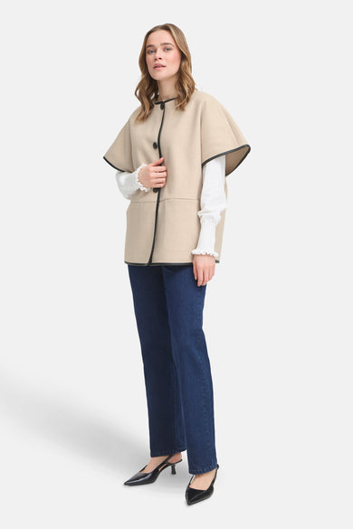 Manteau beige de France, terminé avec un bord noir, associé à une blouse blanche et des jeans bleu marine.