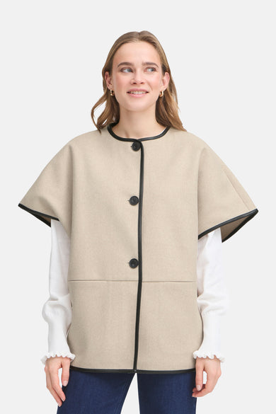 Manteau beige de France, avec des accents noirs le long des bords et porté sur une blouse blanche.