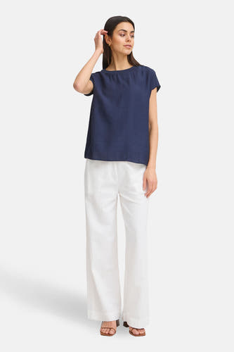 Blauwe blouse met korte mouwen van Fransa, gedragen met witte, wijde broek en sandalen.
