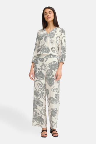 Pantalon écru de France avec imprimé paisley et une blouse coordonnée, associé à des sandales noires.