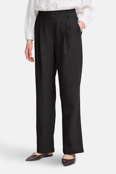 Pantalon noir de France, avec des plis à l'avant et associé à une blouse blanche et des chaussures marrons.
