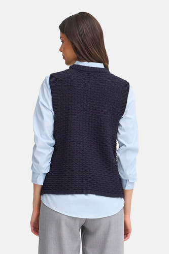 Gilet bleu de France, avec une texture tricotée, porté sur un chemisier bleu clair et un pantalon gris.