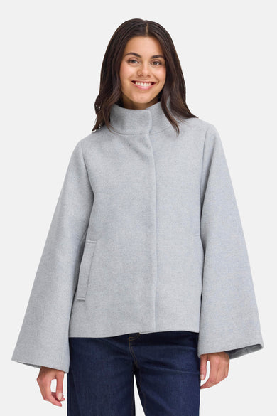 Manteau court gris de France, avec des manches larges et un col montant, porté avec un jean bleu foncé.