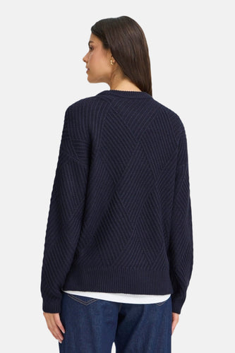 Achterkant van een donkerblauwe gebreide trui met diamantpatroon, gedragen door een vrouw.