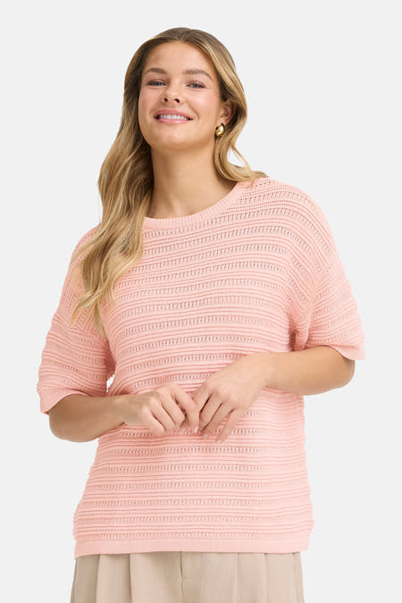 Roze trui met ronde hals van Fransa, met een opengebreide textuur, gecombineerd met een gouden oorbel.
