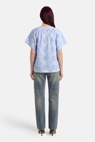 Chemisier bleu à manches courtes de Fransa avec broderie florale blanche, vu de dos. Porté avec un jean délavé et des talons noirs.