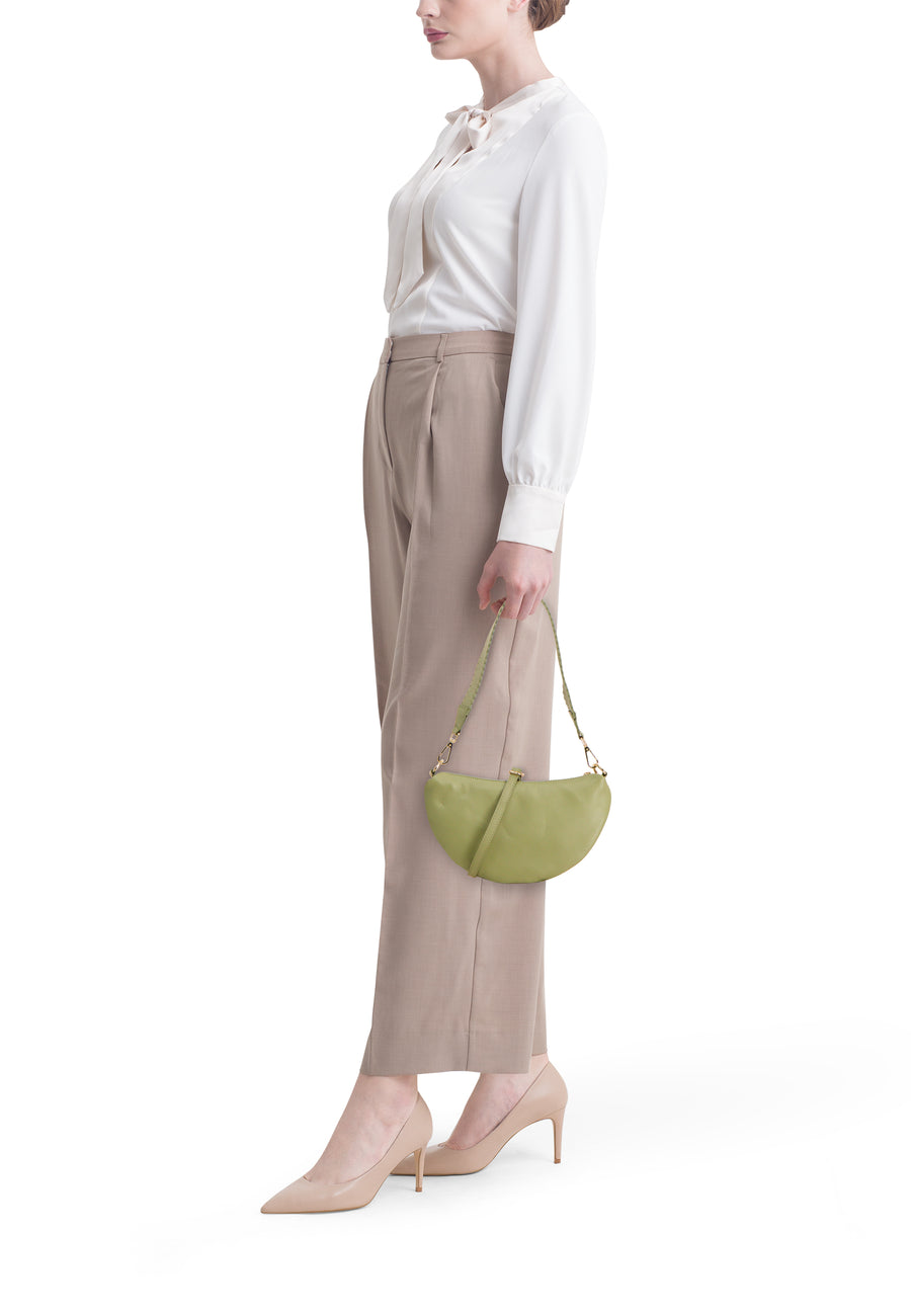 Sac bandoulière vert pour femme Access®, forme demi-lune, en cuir texturé, porté par un mannequin avec une blouse blanche et un pantalon beige.