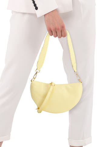 Sac bandoulière pour femme de couleur jaune d'Access® en forme de demi-lune, avec bandoulière amovible à bord festonné et ferrures dorées, porté avec un tailleur blanc.