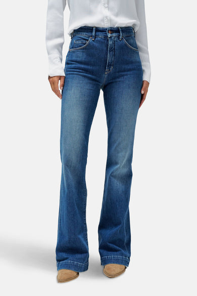 Jean flare en denim bleu moyen de Salsa Jeans, portés avec une blouse blanche et des chaussures marrons.