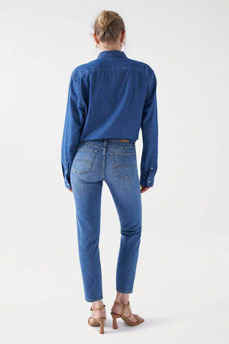Jean slim bleu clair de Salsa Jeans, vu de de derrière, associé à une blouse en denim et des talons hauts.