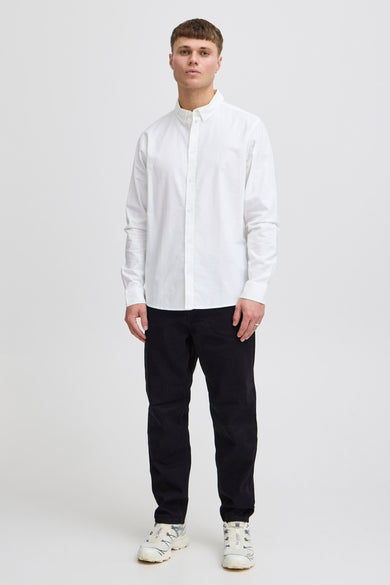 Chemise blanche à manches longues de SOLID, portée avec un pantalon noir et des baskets blanches.