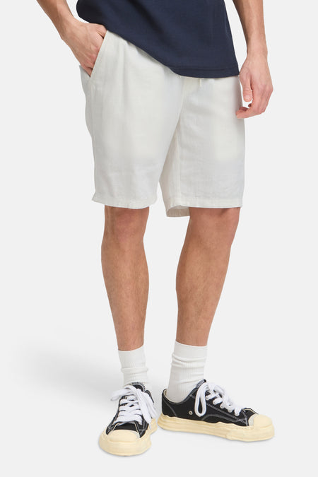 Short en lin de couleur crème de SOLID avec taille à cordon de serrage, porté par un homme en T-shirt bleu foncé et baskets.