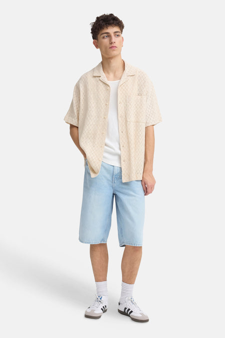 Short en jean bleu clair de SOLID, porté par un homme avec une chemise beige et des baskets blanches.