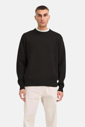 Pull noir avec col rond de SOLID, porté avec un T-shirt blanc et un pantalon beige.