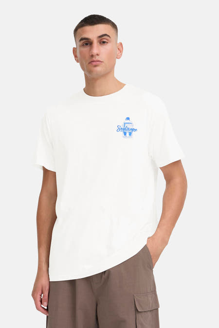 T-shirt blanc à manches courtes de SOLID, avec imprimé bleu, porté avec un pantalon cargo marron et des baskets blanches.