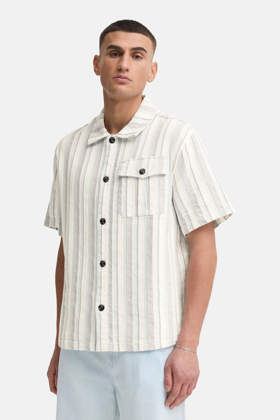 Chemise à manches courtes rayée beige et blanc de SOLID, avec col à revers et poche poitrine, portée avec un short bleu clair et des sabots en daim.