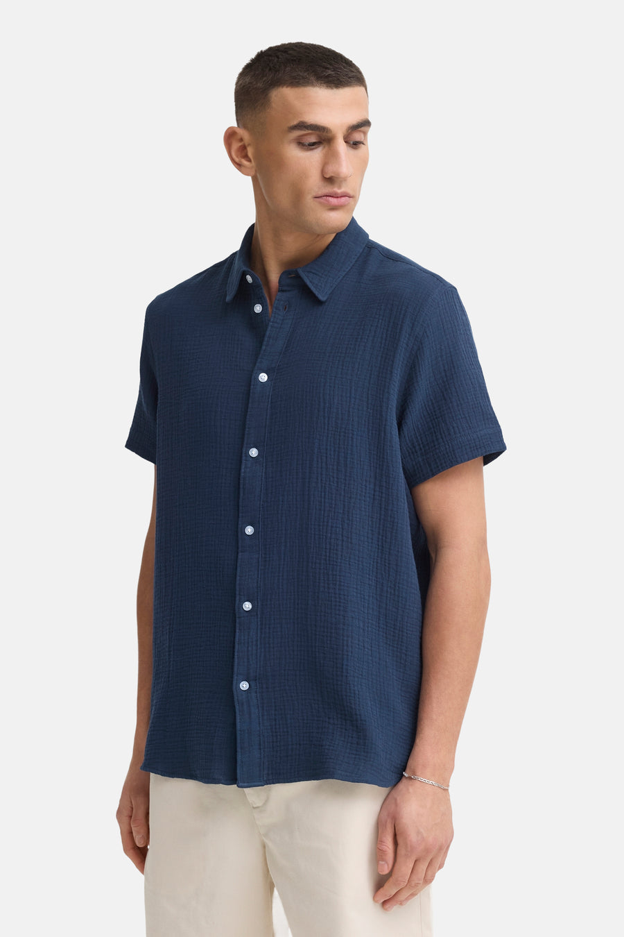 Chemise bleue à manches courtes de SOLID, en tissu texturé, associée à un short beige et des sabots en daim.