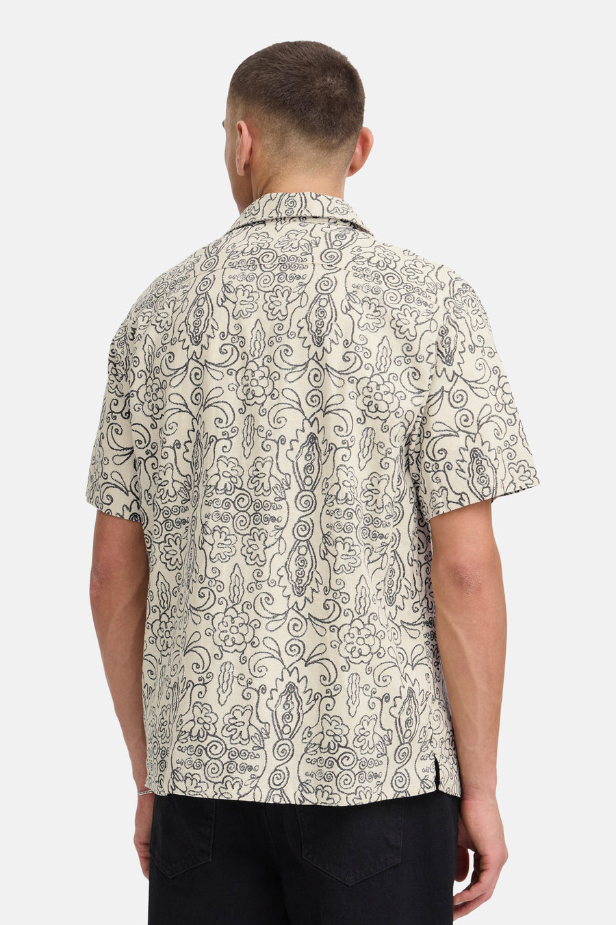 Chemise écru à manches courtes de SOLID, avec motif abstrait bouclé gris foncé, vue de dos avec un jean noir et un bracelet argenté.