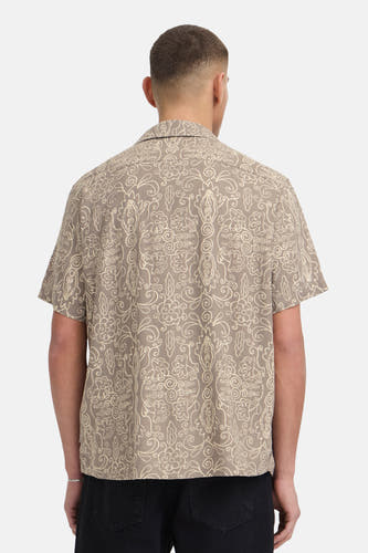 Chemise marron à manches courtes de SOLID, avec motif décoratif blanc cassé, portée par un homme vu de dos avec un pantalon noir et un bracelet argenté.