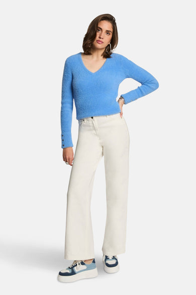 Pull-over V-hals bleu de Morgan De Toi, avec des manches longues et des détails à boutons, associé à un pantalon blanc et des baskets bleues.