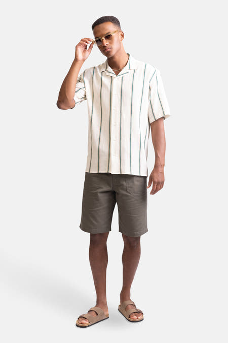 Chemise écru à manches courtes de REDEFINED REBEL, avec des rayures verticales vert et portée avec un short et des sandales.