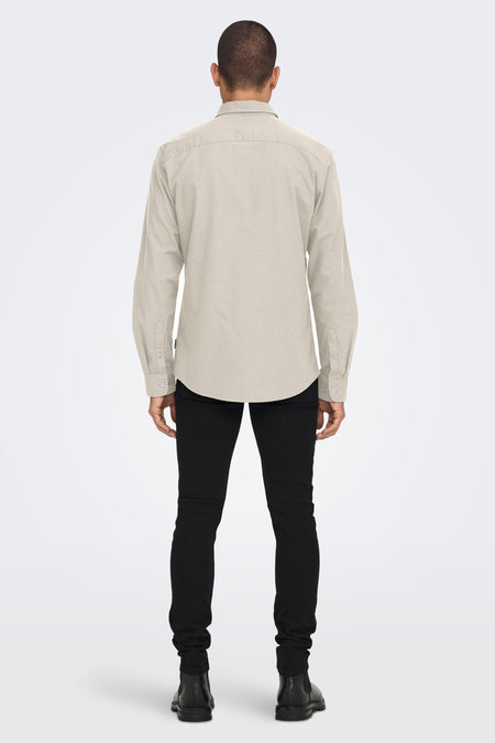 Achterkant van een man in een beige overhemd, zwarte broek en zwarte laarzen tegen een witte achtergrond.