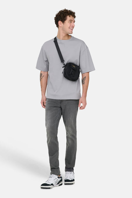 Grijze slim fit jeans van ONLY & SONS®, met een subtiele wassing en gecombineerd met een grijze t-shirt en zwarte schoudertas.
